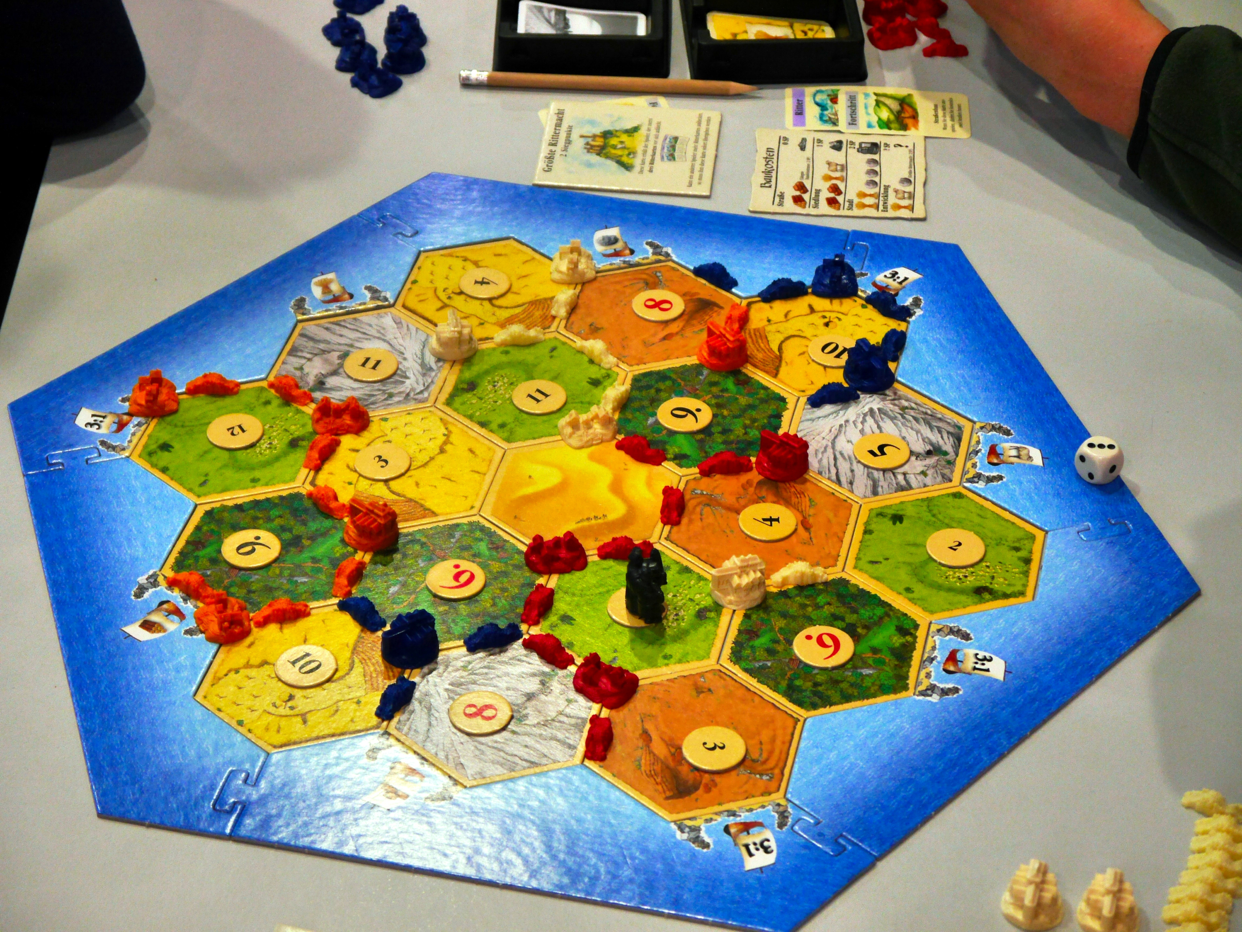 Brettspiel Siedler von Catan mit verschiedenen Spielsteinen und einem Würfel auf einem Tisch.