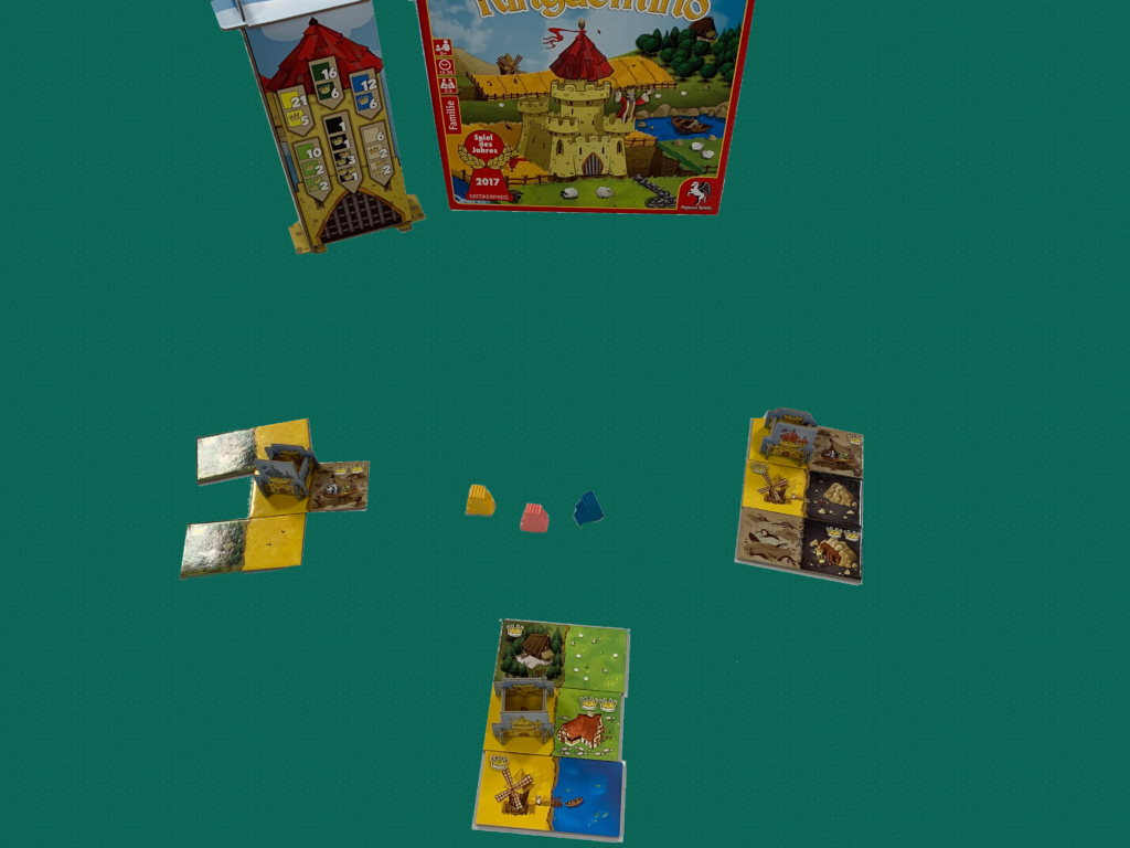 Kingdomino Brettspiel mit Spielsteinen und Spielbox auf grünem Hintergrund.