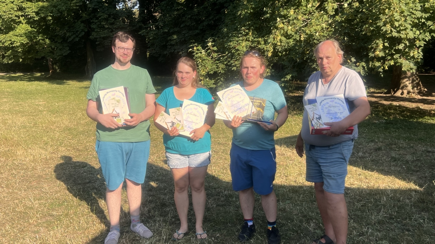 Vier Personen stehen im Freien und halten Brettspiele in den Händen.