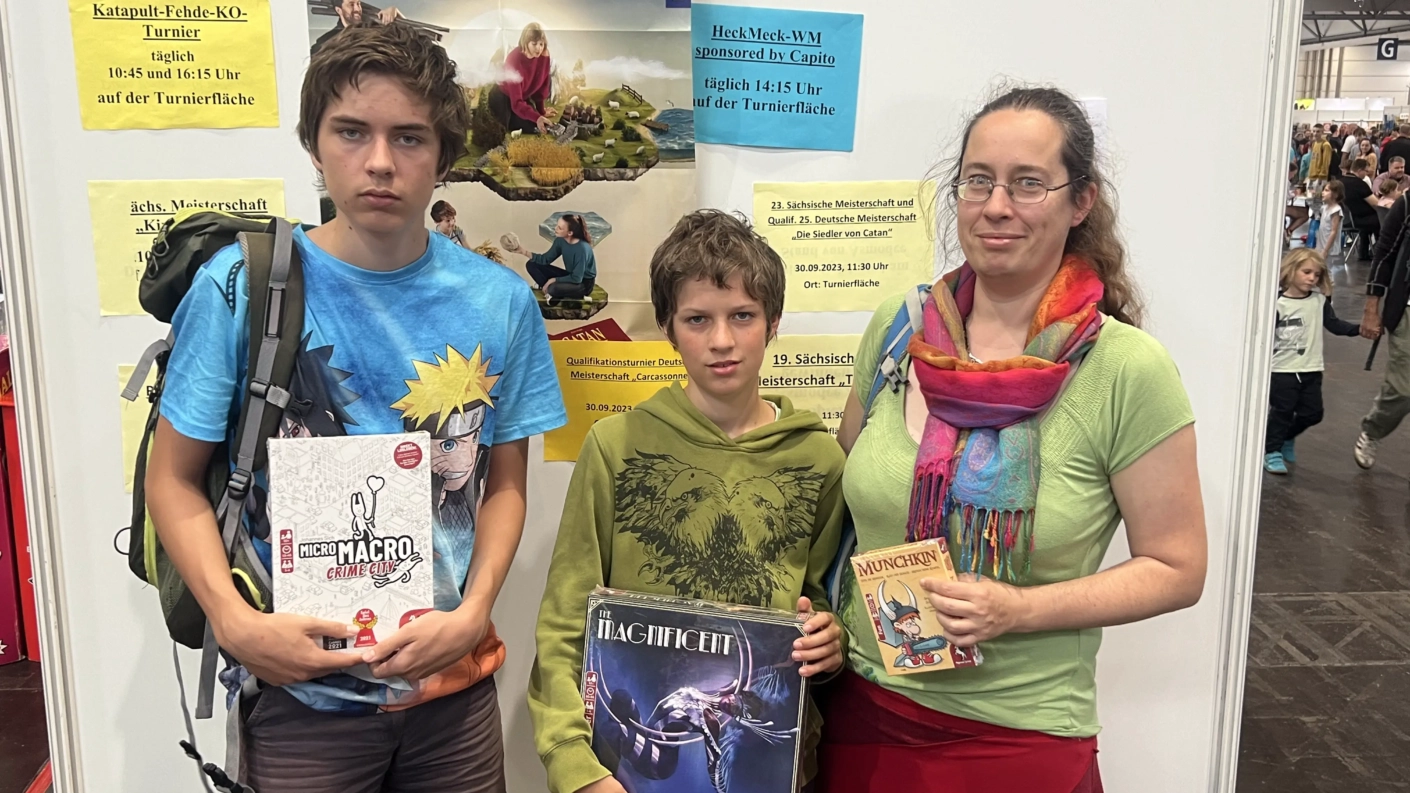 Familie steht an einem Stand mit Brettspielen und hält verschiedene Spiele in den Händen.