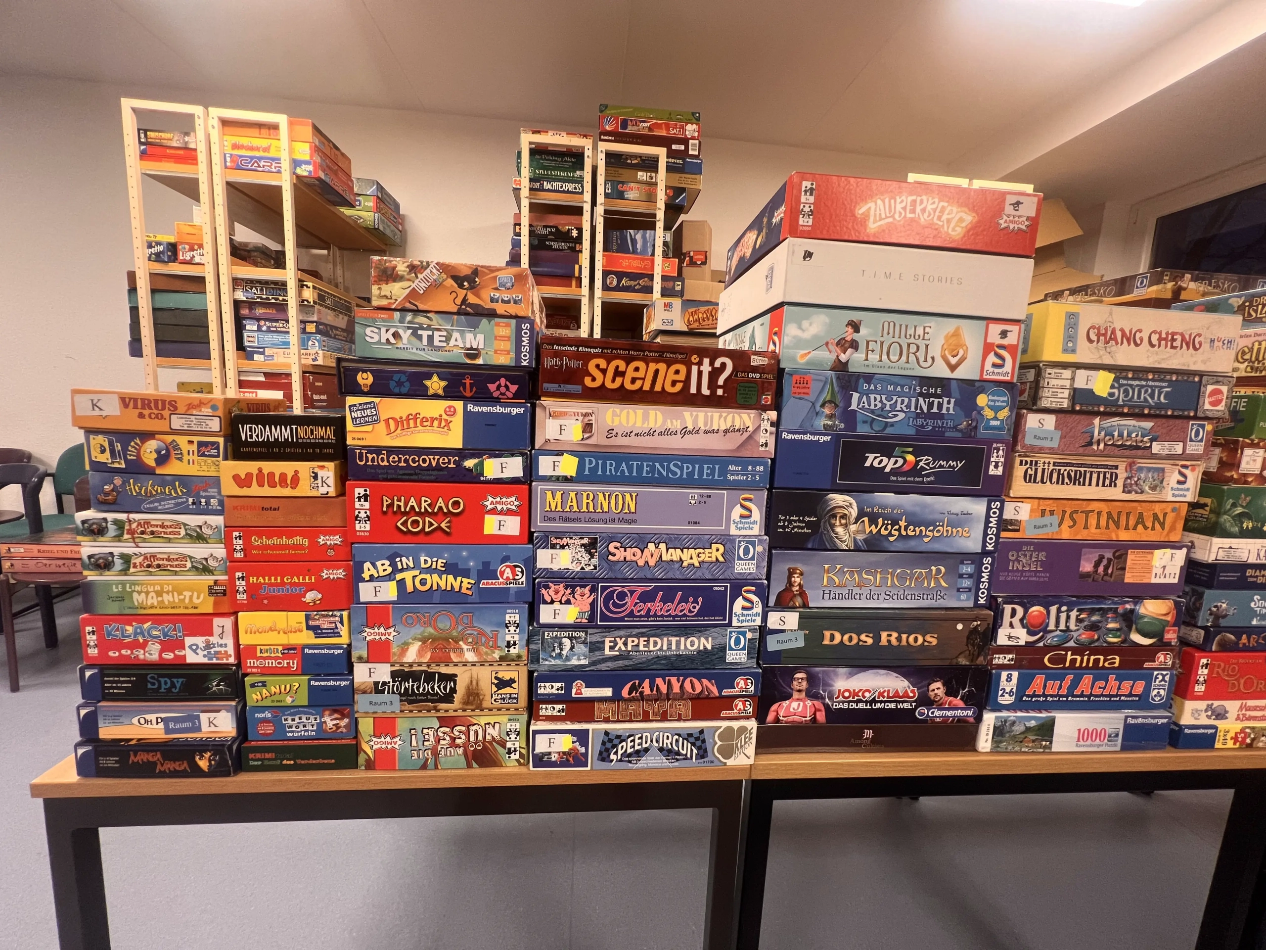 Eine Vielzahl von Brettspielen, die auf einem Tisch gestapelt sind, mit verschiedenen Titeln und Designs sichtbar.