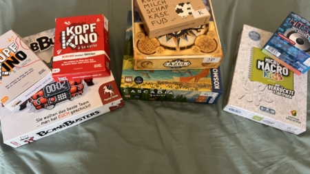 Verschiedene Brettspiele auf einem Bett, darunter Kopfkino, Cascadia und Azuls.