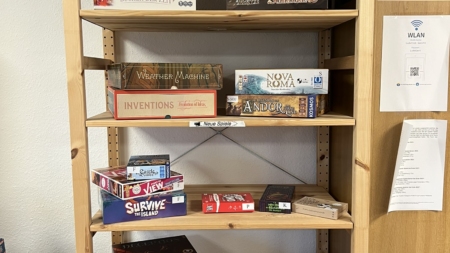 Holzregal mit verschiedenen Brettspielen, darunter Plague Inc. und Carnegie.