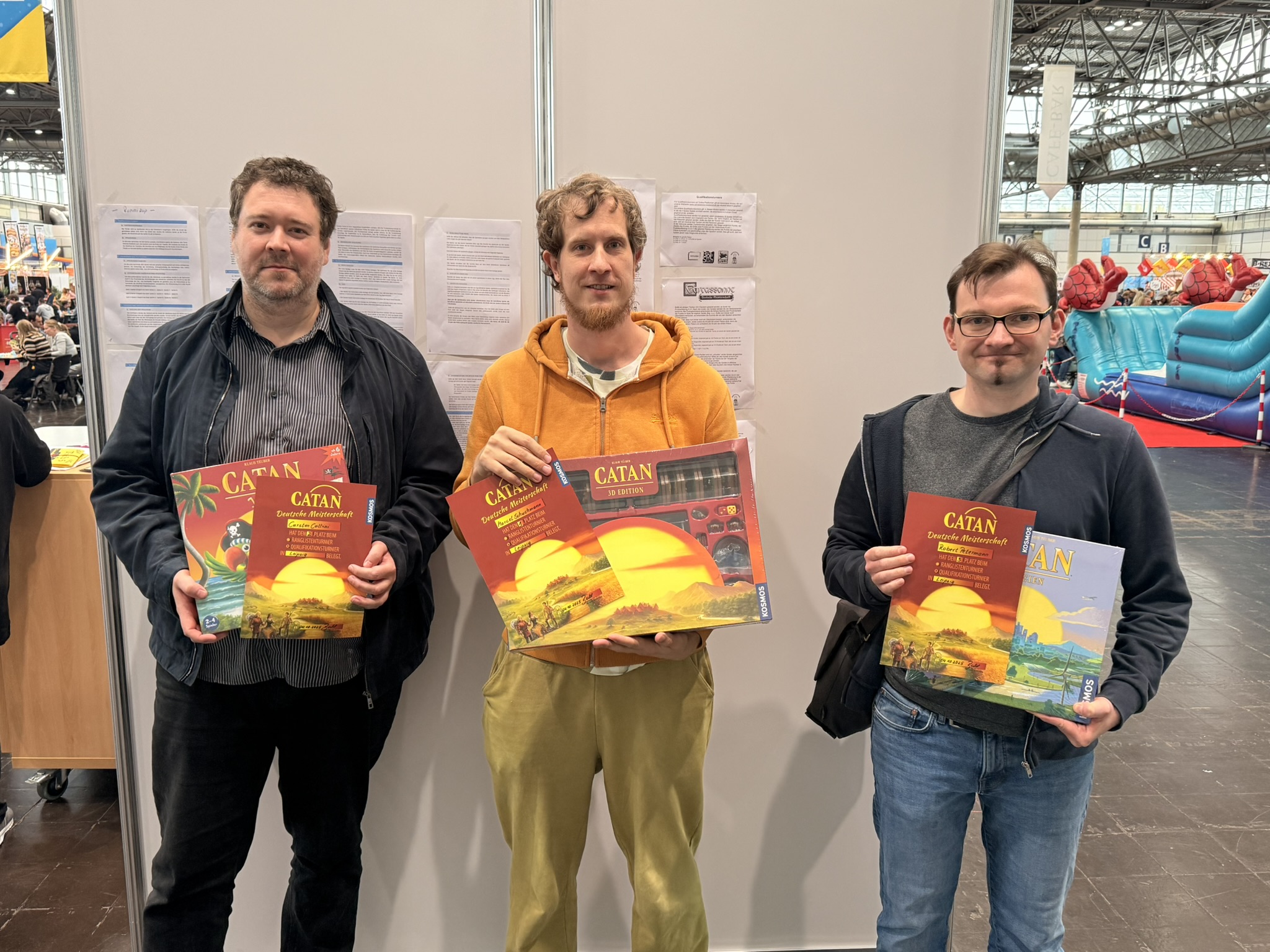 Drei Männer halten verschiedene Editionen des Brettspiels Catan in den Händen.