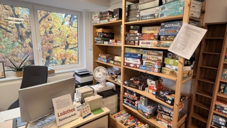 Holzregal mit verschiedenen Brettspielen in der Ludothek Leipzig, darunter bekannte Titel und Spieleboxen.
