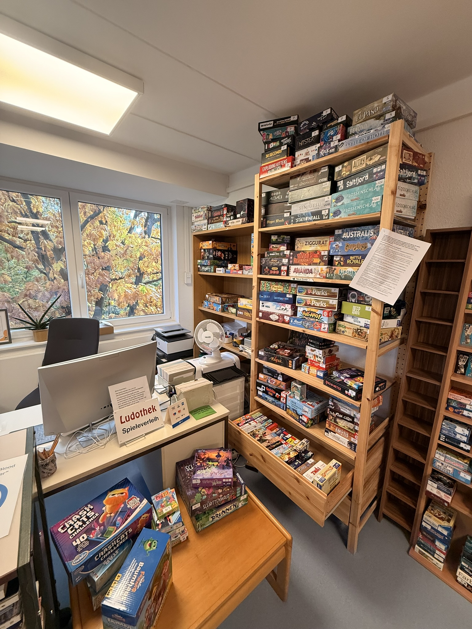 Holzregal mit verschiedenen Brettspielen in der Ludothek Leipzig, darunter bekannte Titel und Spieleboxen.