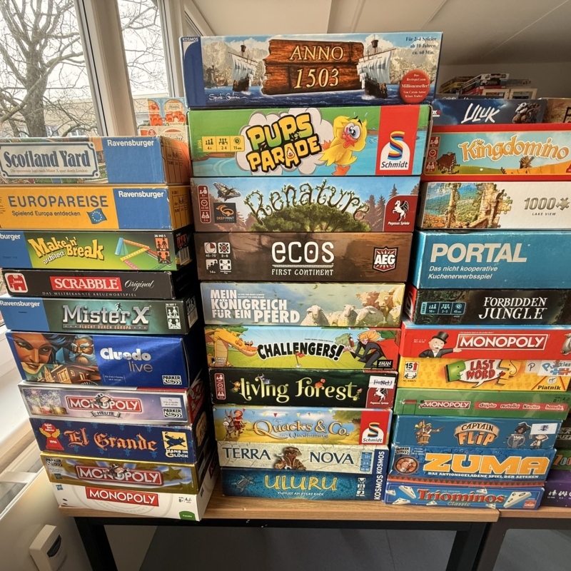Brettspiele auf einem Tisch, darunter Anno 1503, Pups Parade, und Monopoly, ordentlich gestapelt.