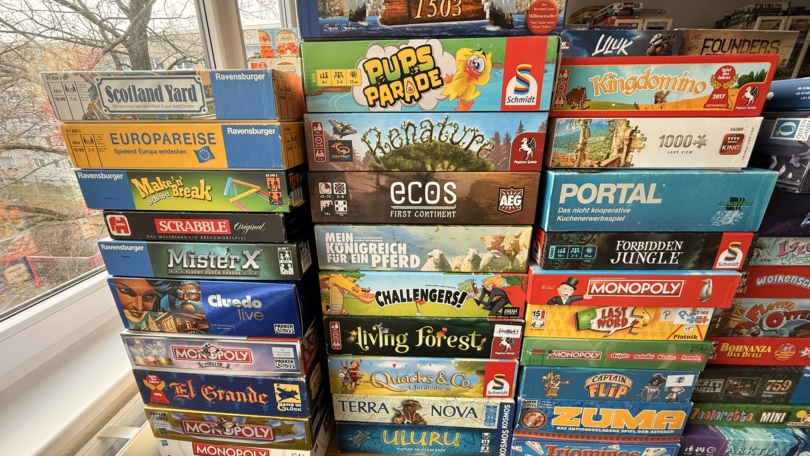 Brettspiele auf einem Tisch, darunter Anno 1503, Pups Parade, und Monopoly, ordentlich gestapelt.
