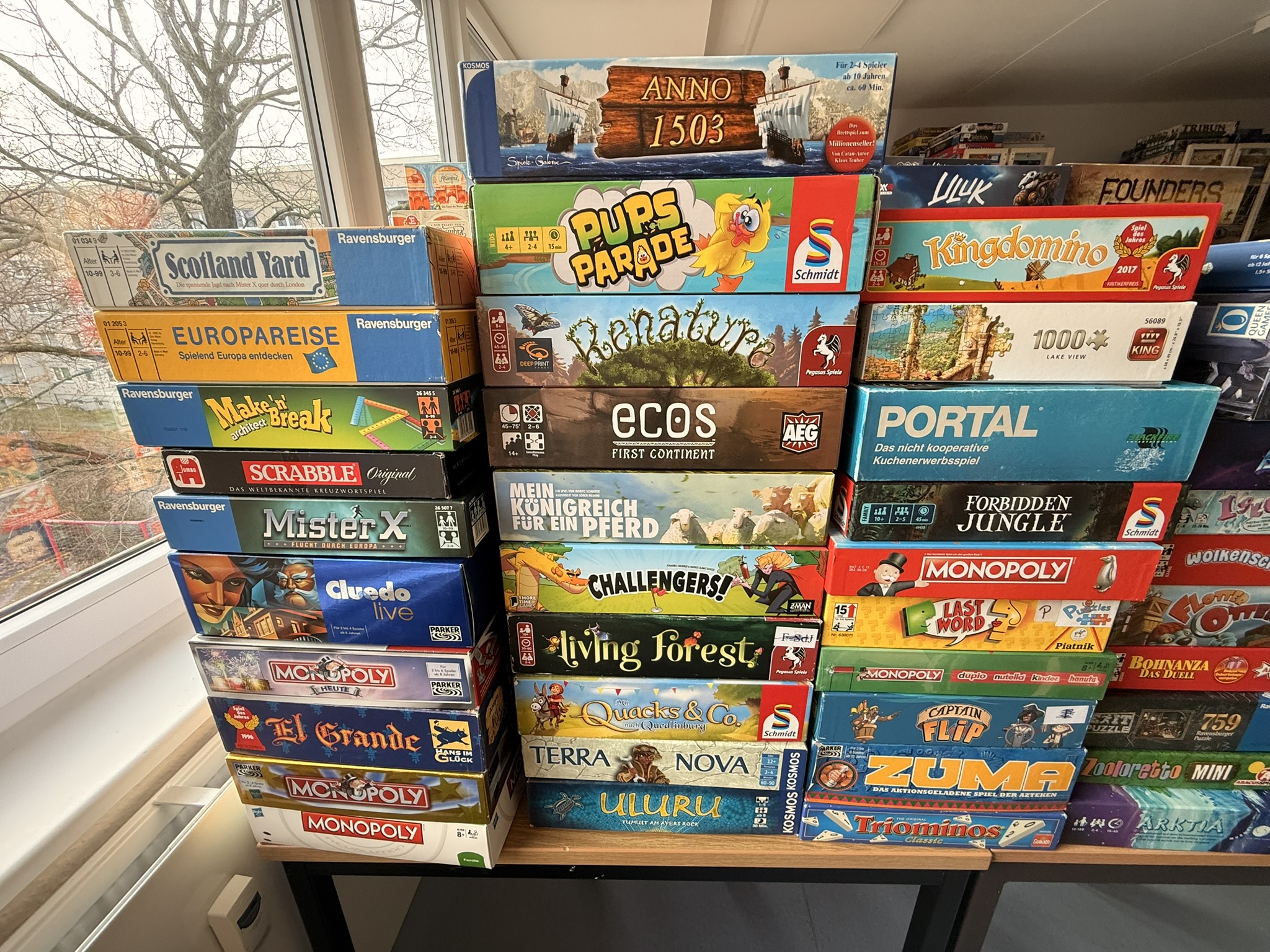 Brettspiele auf einem Tisch, darunter Anno 1503, Pups Parade, und Monopoly, ordentlich gestapelt.
