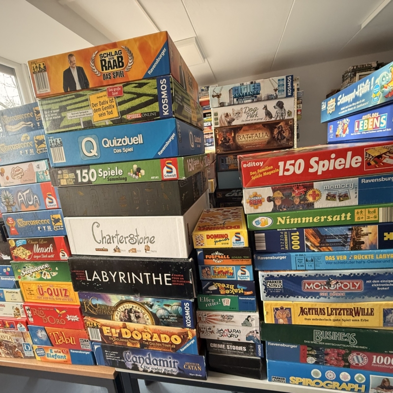 Stapel von verschiedenen Brettspielen in einer Spielebibliothek mit bunten Verpackungen.
