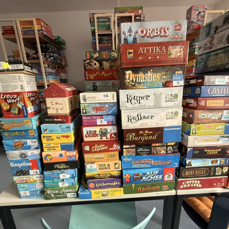 Verschiedene Brettspiele in einer gestapelten Anordnung auf einem Tisch im Sächsischen Spielezentrum.