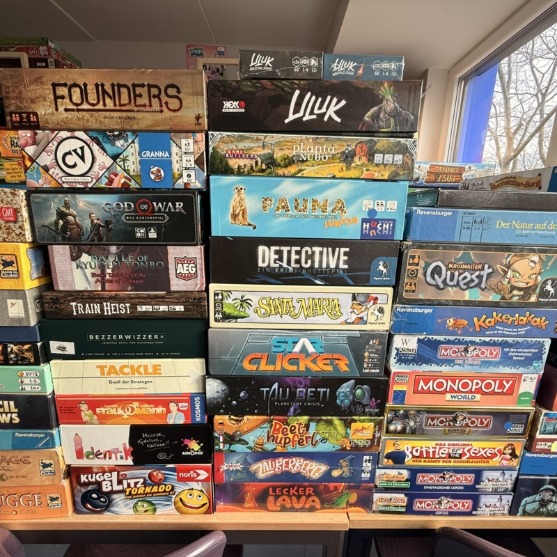 Eine Vielzahl von Brettspielen in einer gestapelten Anordnung in einem Innenraum.