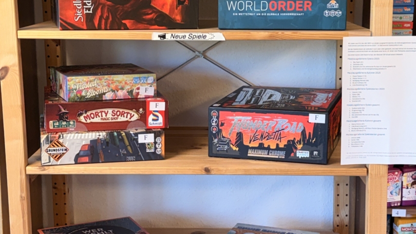 Mehrere Brettspiele zu den neuen Spielen Februar bis April 2026 stehen im Regal, darunter Thunder Road: Vendetta Maximum Chrome, World Order und Railroad Tiles.