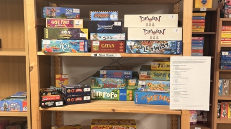 Auf einem Holzregal stehen im Sächsischen Spielezentrum zahlreiche neue Brettspiele wie Catan, Wilmot's Warehouse und Echos der Zeit nebeneinander.