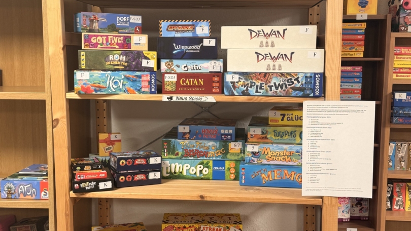 Auf einem Holzregal stehen im Sächsischen Spielezentrum zahlreiche neue Brettspiele wie Catan, Wilmot's Warehouse und Echos der Zeit nebeneinander.