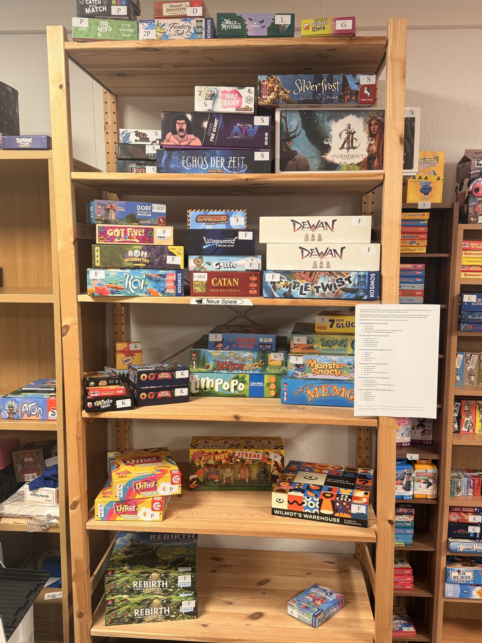 Auf einem Holzregal stehen im Sächsischen Spielezentrum zahlreiche neue Brettspiele wie Catan, Wilmot's Warehouse und Echos der Zeit nebeneinander.
