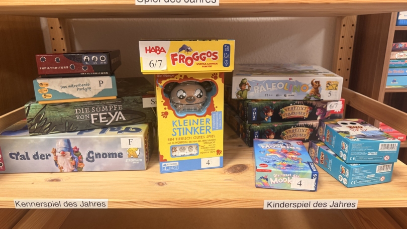 Unter dem Schild „Spiel des Jahres“ stehen Brettspielboxen wie Wilmot’s Warehouse, Froggos, Kleiner Stinker und Paleolino im Regal im Juni 2026.