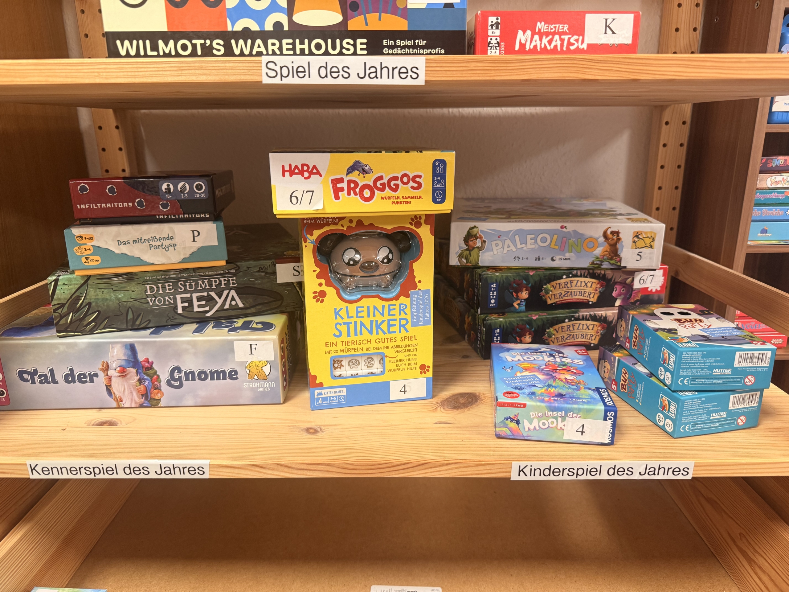 Unter dem Schild „Spiel des Jahres“ stehen Brettspielboxen wie Wilmot’s Warehouse, Froggos, Kleiner Stinker und Paleolino im Regal im Juni 2026.