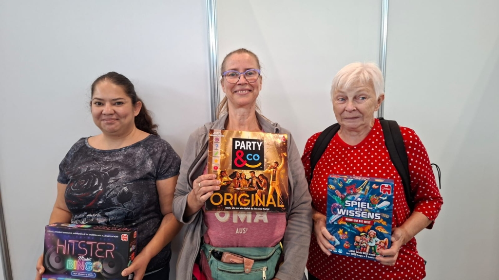 Drei Teilnehmerinnen der Hobbymesse 2026 präsentieren Brettspiele wie Hitster, Party & Co. und Spiel des Wissens.