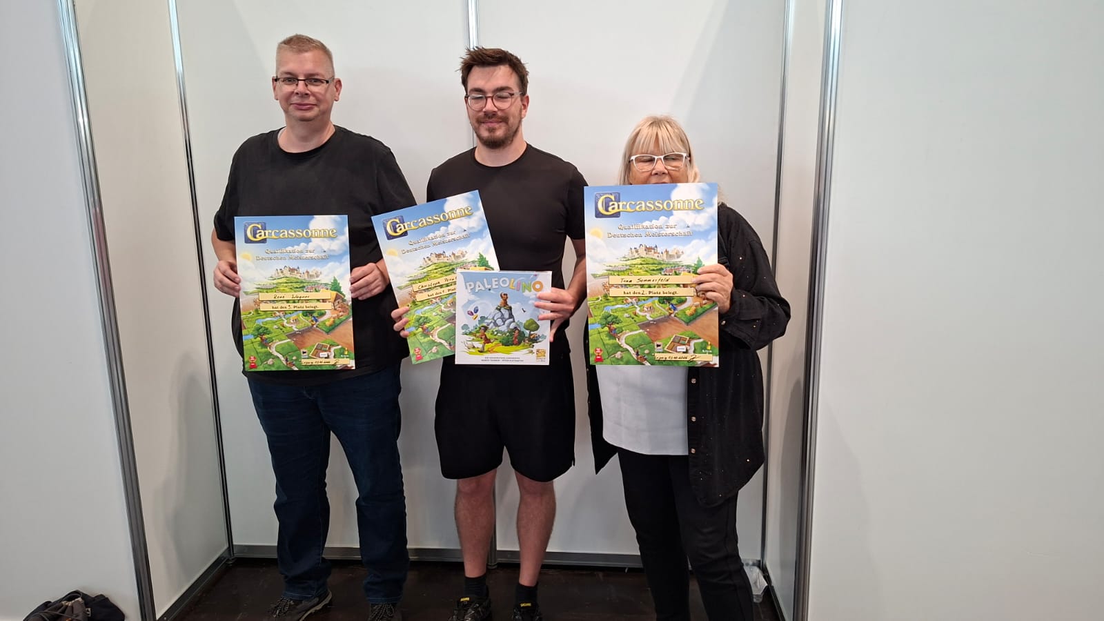 Drei Gewinner des Carcassonne-Qualifikationsturniers 2026 zeigen ihre Spielepreise nach dem Turnier auf der Hobbymesse.