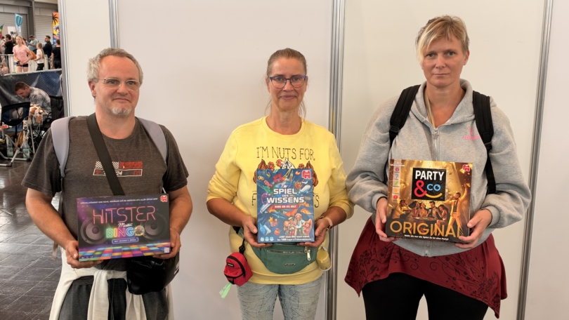 Drei Teilnehmende der Hobbymesse 2026 zeigen Gesellschaftsspiele: „Hitster Music Bingo“, „Spiel des Wissens“ und „Party & Co Original“.